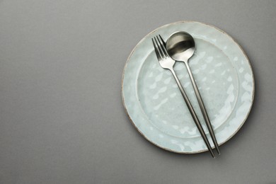 Clean plate, fork and spoon on grey background, top view. Space for text