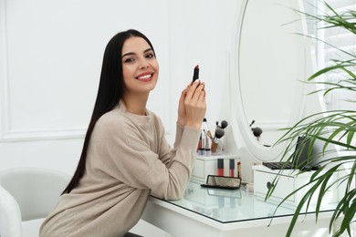 Beautiful woman applying makeup near mirror in room