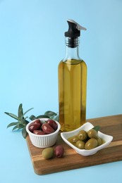 Photo of Bottle of oil, olives and tree twig on light blue background