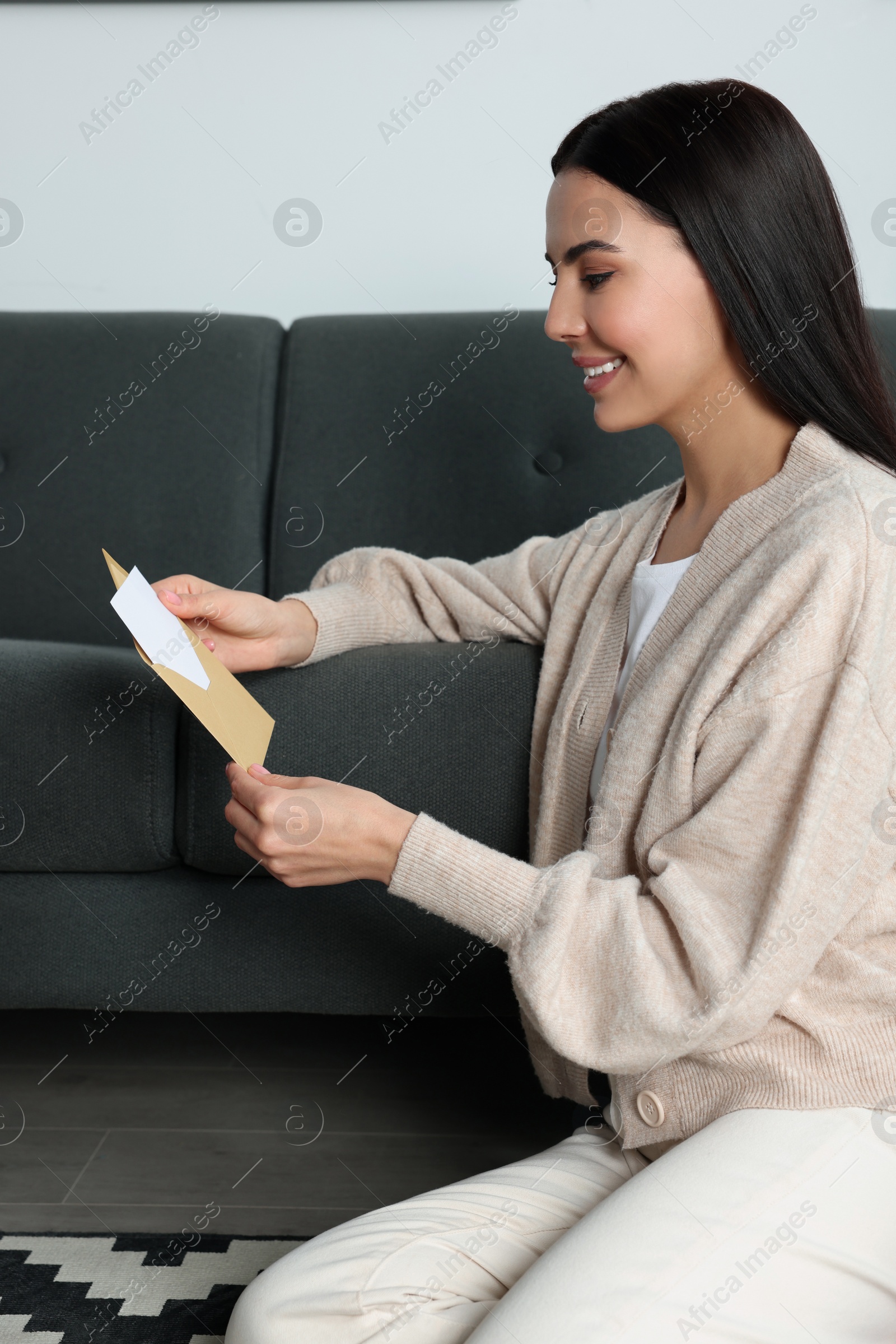 Photo of Happy woman reading greeting card on floor in living room