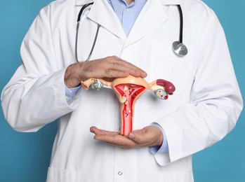 Photo of Doctor demonstrating model of female reproductive system on light blue background, closeup. Gynecological care
