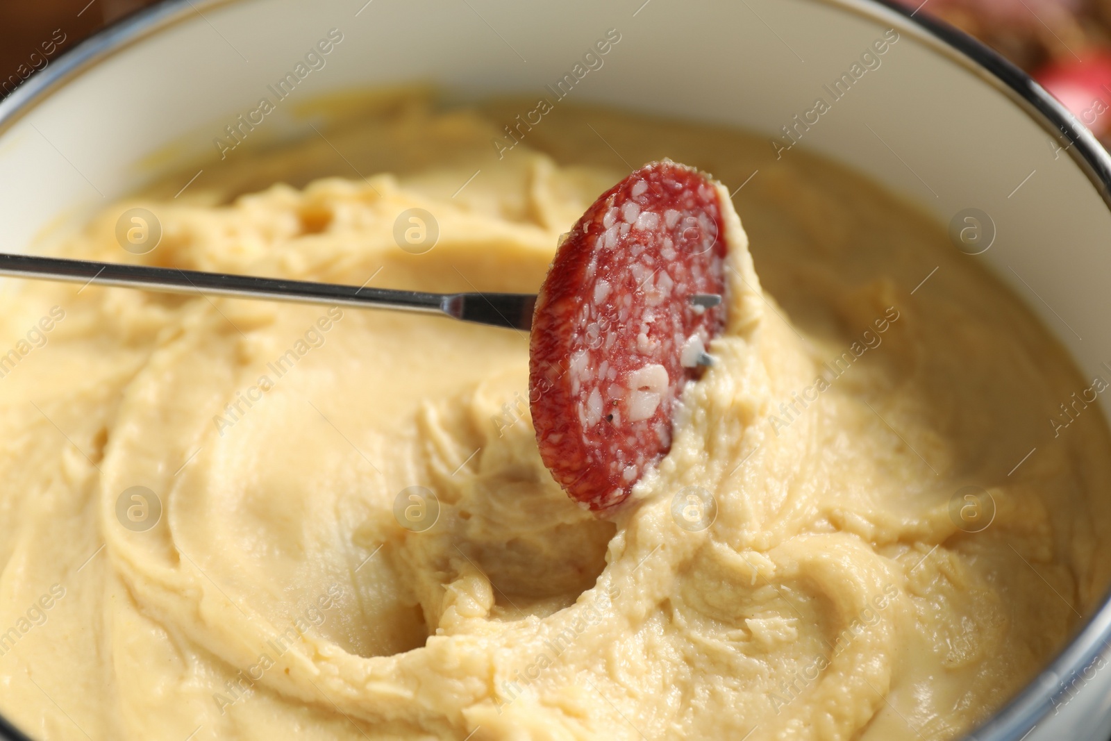 Photo of Dipping piece of sausage into fondue pot with melted cheese, closeup