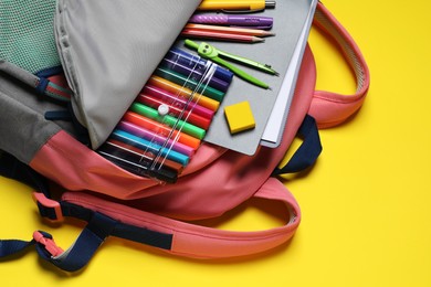 Photo of Backpack with school stationery on yellow background, closeup