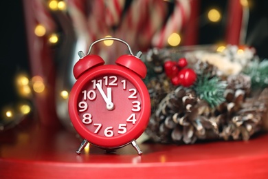 Photo of Alarm clock and decor on red table against blurred Christmas lights. New Year countdown