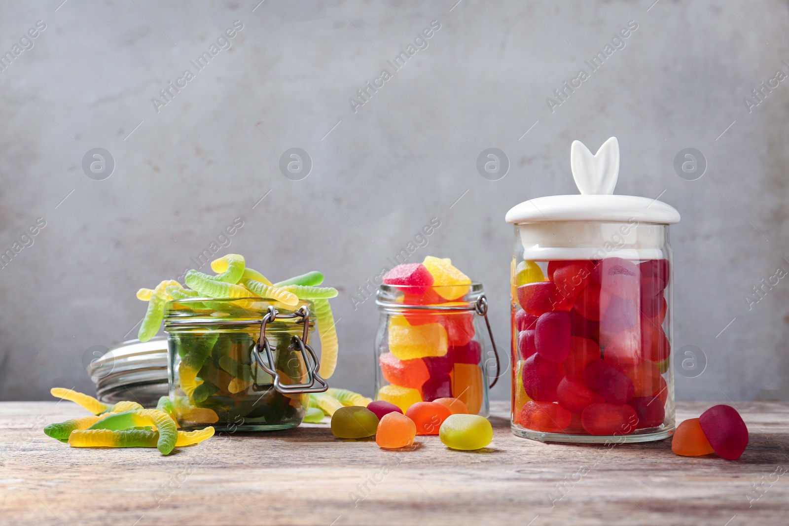 Photo of Glass jars and tasty jelly candies on wooden table against light background, space for text