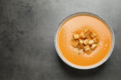 Photo of Tasty creamy pumpkin soup with croutons in bowl on grey table, top view. Space for text