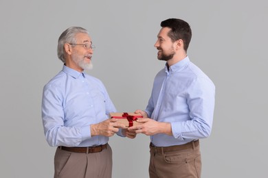 Son giving gift box to his dad on gray background