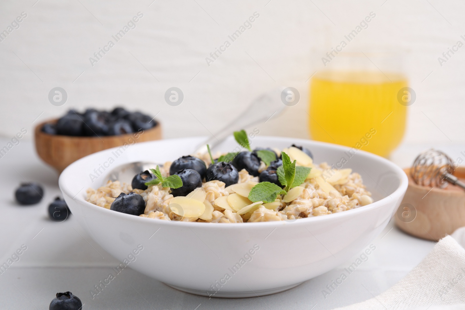 Photo of Tasty oatmeal with blueberries, mint and almond petals in bowl on white tiled table