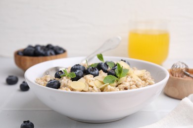 Photo of Tasty oatmeal with blueberries, mint and almond petals in bowl on white tiled table