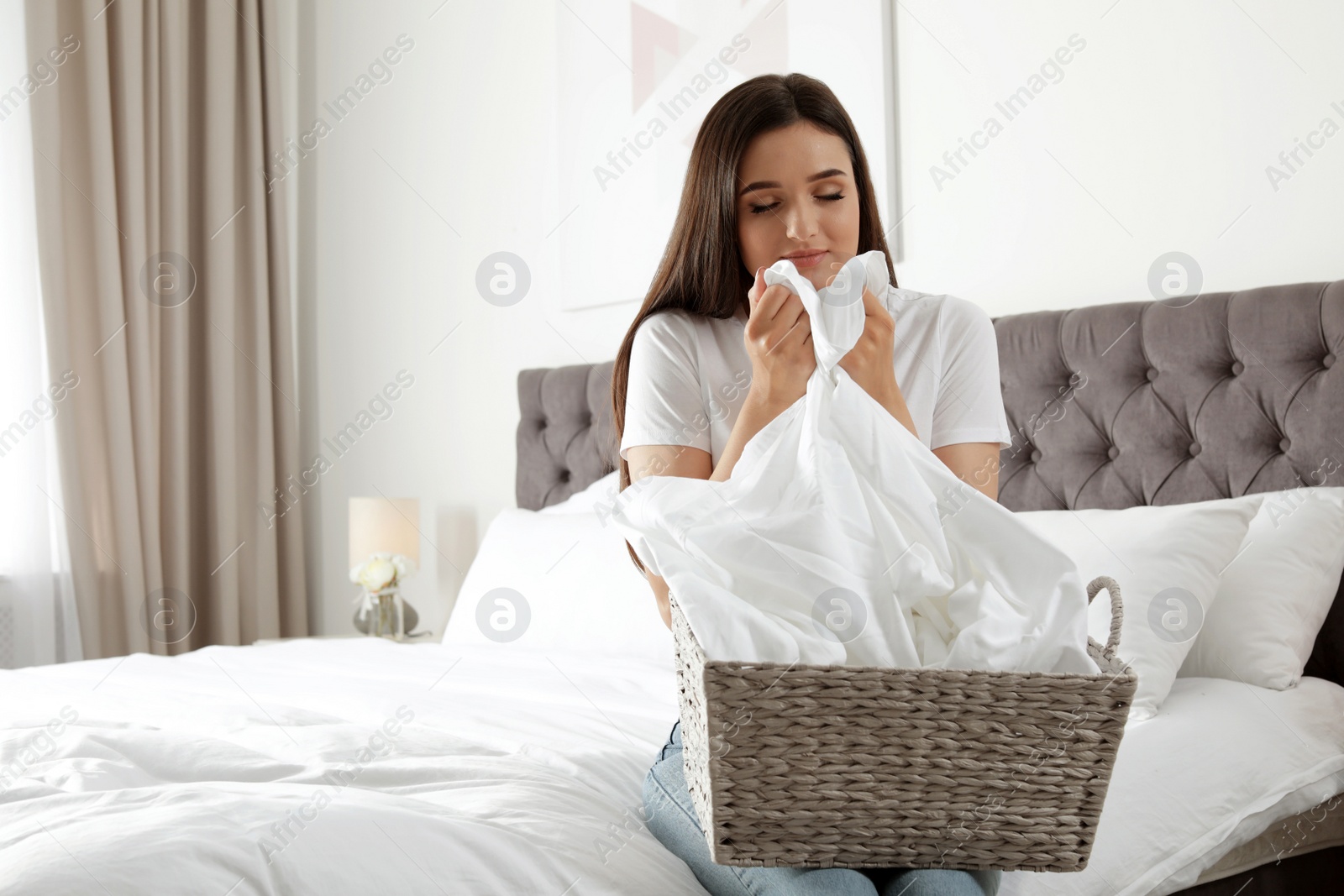 Photo of Young woman smelling fresh laundry in bedroom. Space for text