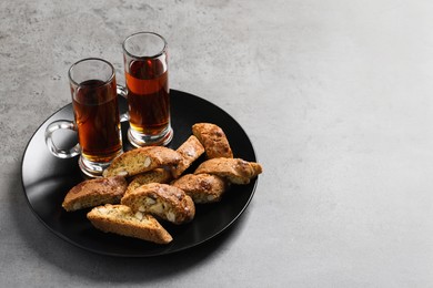 Tasty cantucci and glasses of liqueur on grey table, space for text. Traditional Italian almond biscuits