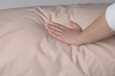 Photo of Woman touching soft beige pillow on bed, closeup