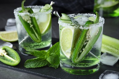 Photo of Spicy cocktail with jalapeno, cucumber and lime on black table, closeup