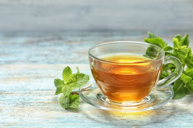 Photo of Cup with hot aromatic mint tea and fresh leaves on wooden table