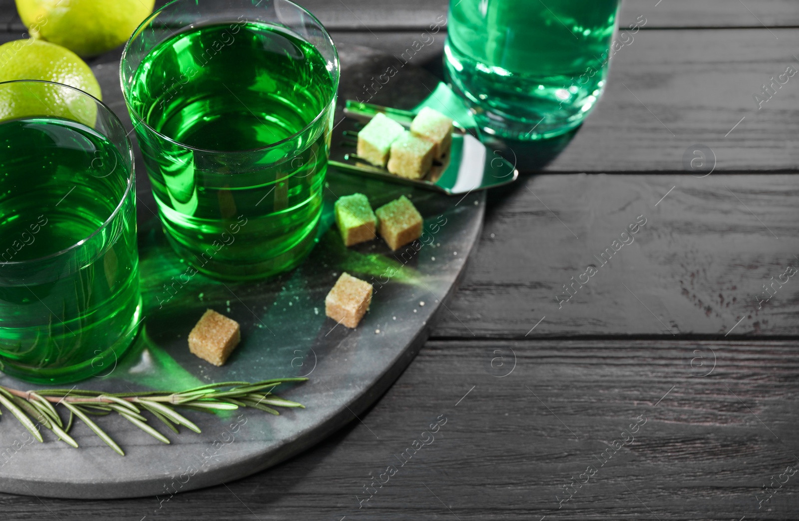 Photo of Absinthe in glasses, rosemary, brown sugar and lime on black wooden table, space for text. Alcoholic drink