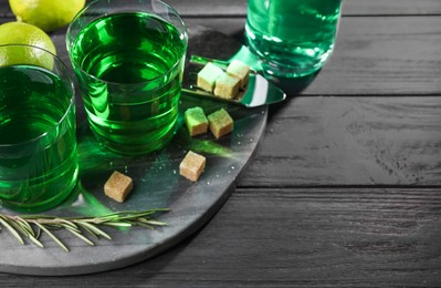 Photo of Absinthe in glasses, rosemary, brown sugar and lime on black wooden table, space for text. Alcoholic drink