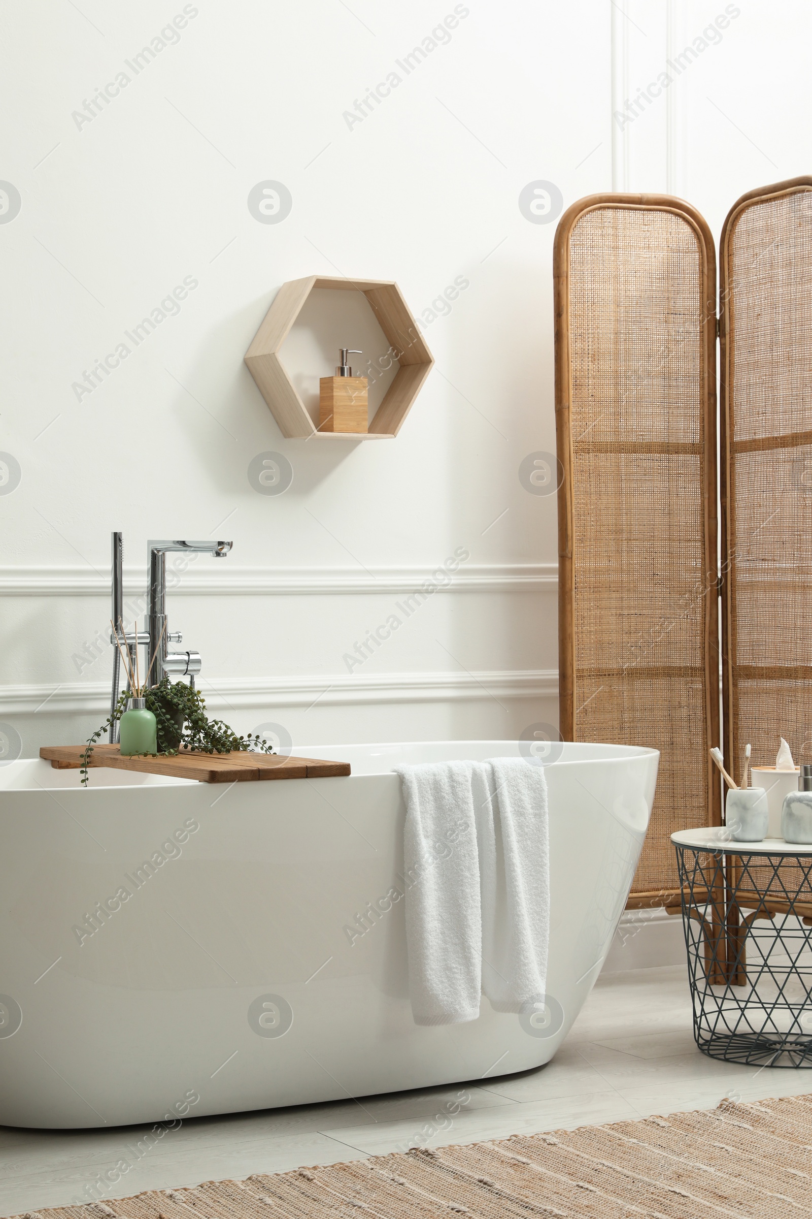 Photo of Modern ceramic bathtub and green plant near white wall in room