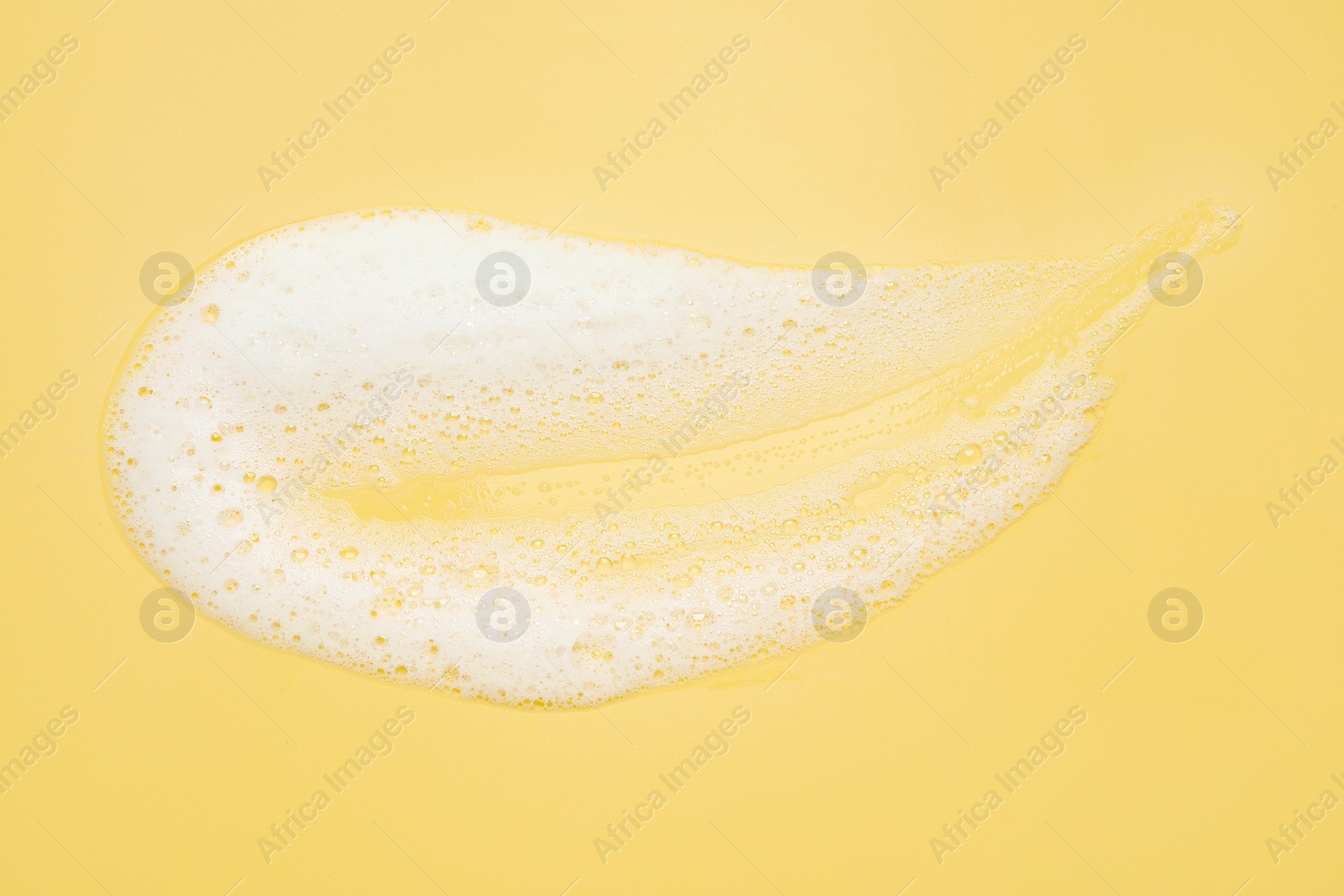 Photo of Smudge of white washing foam on yellow background, top view