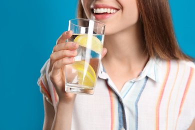 Young woman drinking lemon water on light blue background, closeup