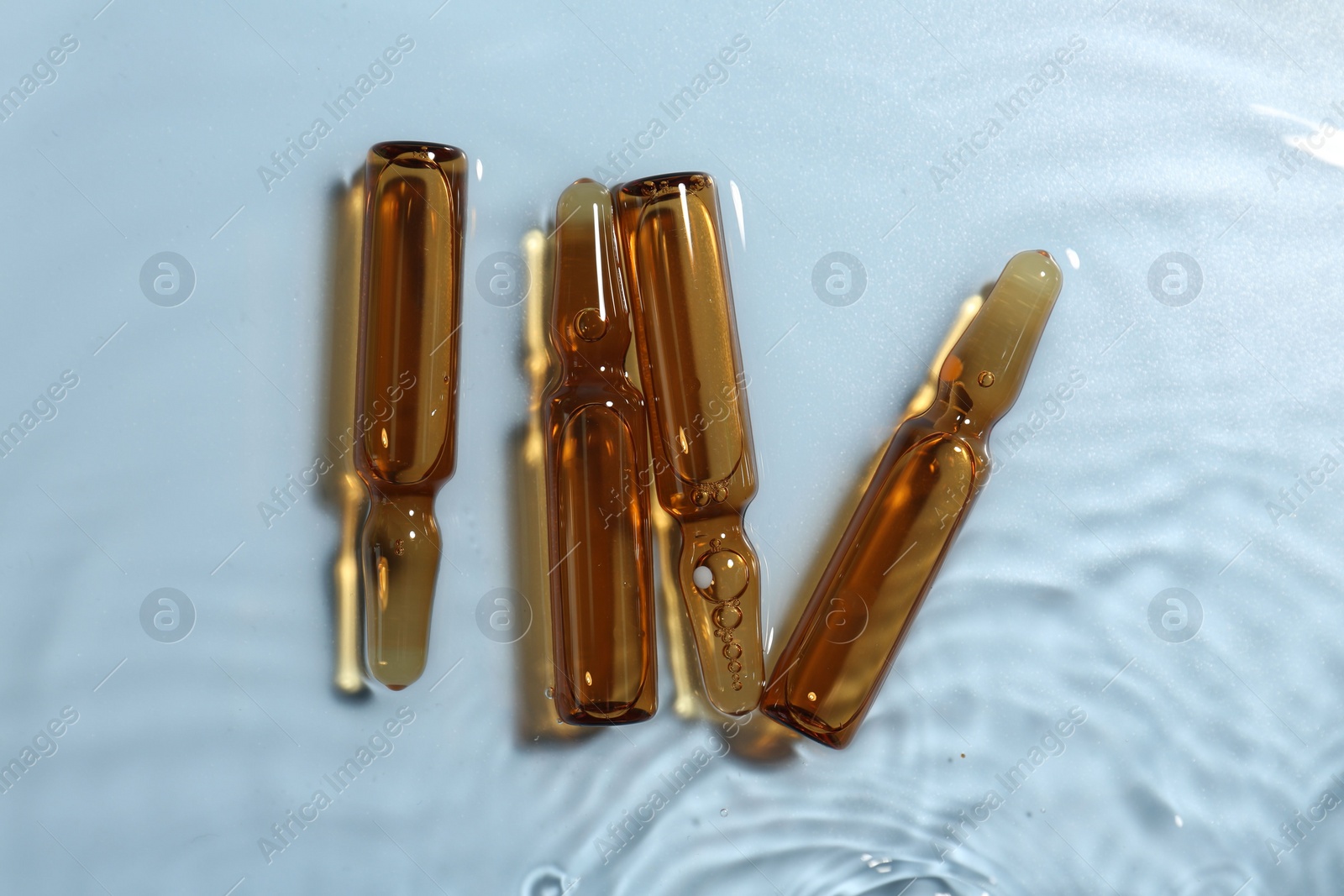 Photo of Skincare ampoules in water on light blue background, top view