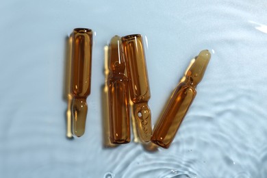 Photo of Skincare ampoules in water on light blue background, top view