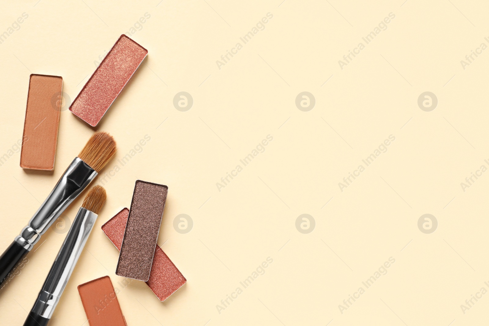 Photo of Different beautiful eye shadows and makeup brushes on beige background, flat lay. Space for text