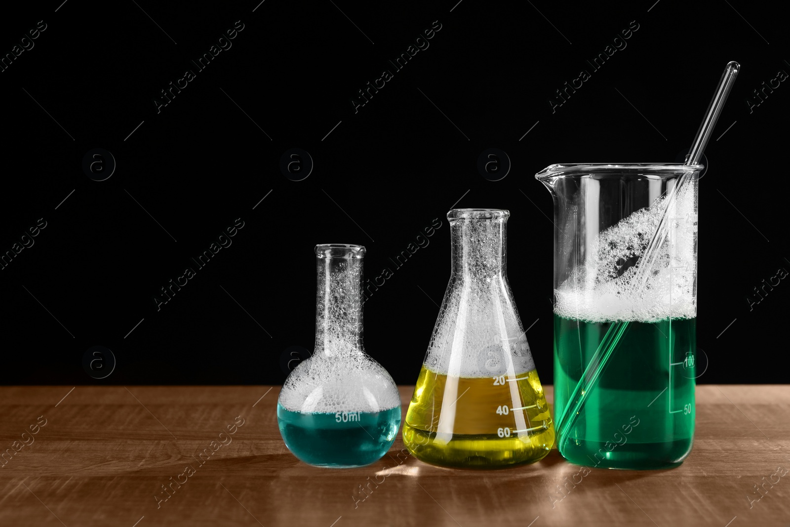 Photo of Laboratory glassware with colorful liquids on wooden table against black background, space for text. Chemical reaction