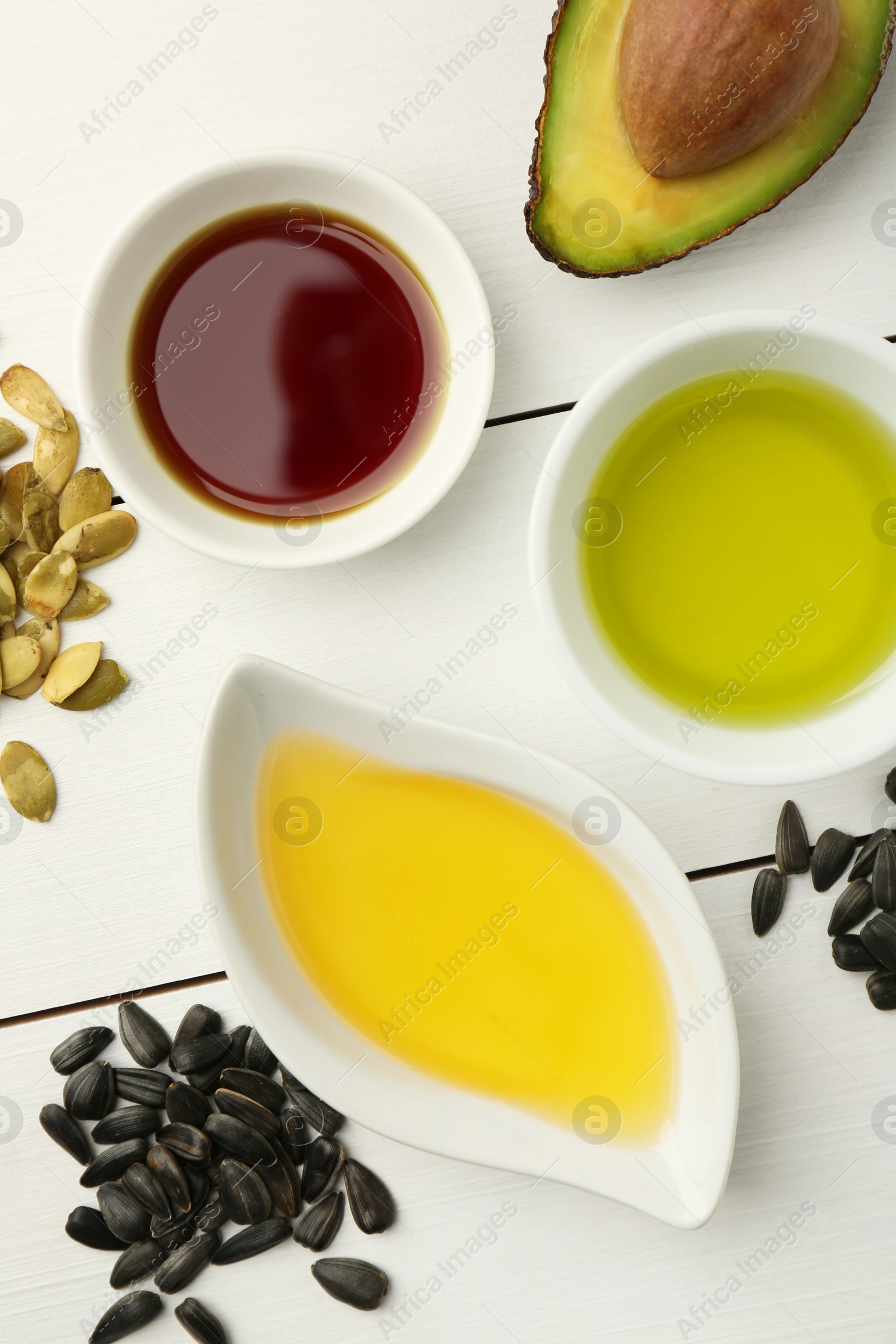 Photo of Vegetable fats. Different cooking oils in bowls and ingredients on white wooden table, flat lay