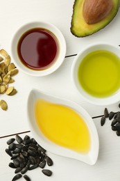 Photo of Vegetable fats. Different cooking oils in bowls and ingredients on white wooden table, flat lay