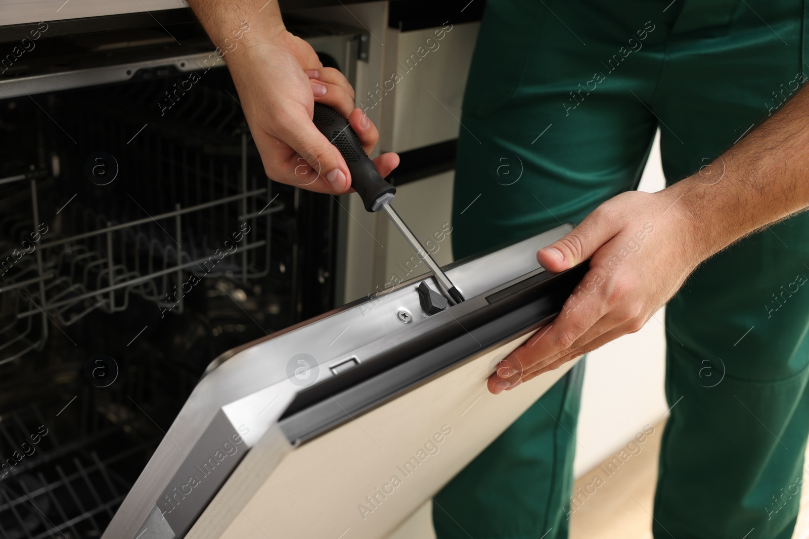 Photo of Serviceman repairing dishwasher door with screwdriver indoors, closeup