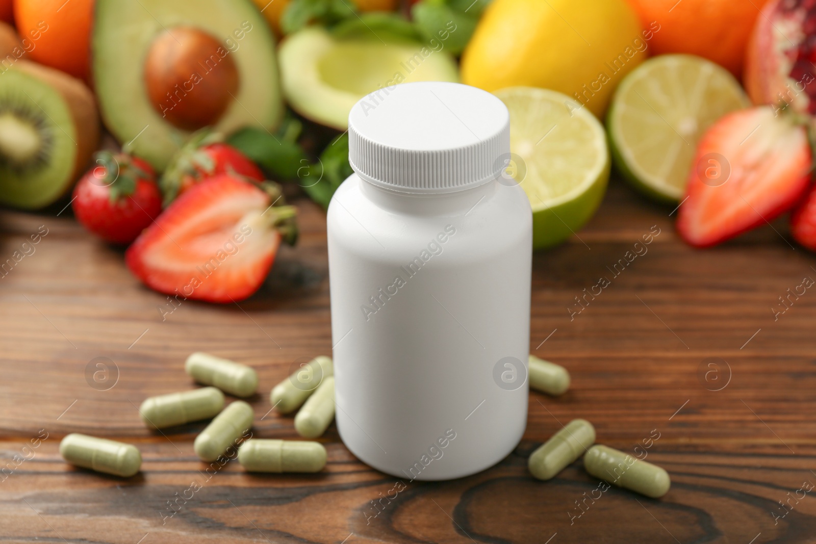 Photo of Vitamin pills, bottle and fresh fruits on wooden table