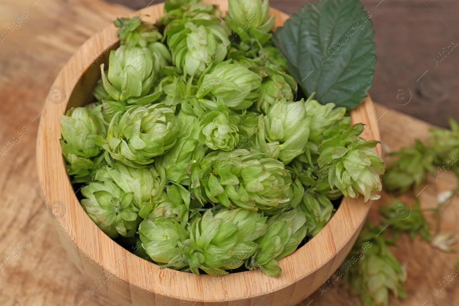 Photo of Bowl of fresh green hops on wooden table, closeup