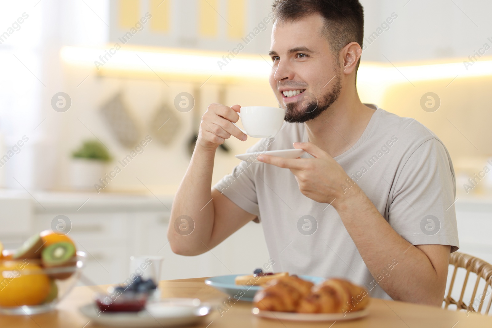 Photo of Smiling man drinking coffee at breakfast indoors