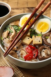 Bowl of delicious ramen and chopsticks on wooden table, closeup. Noodle soup