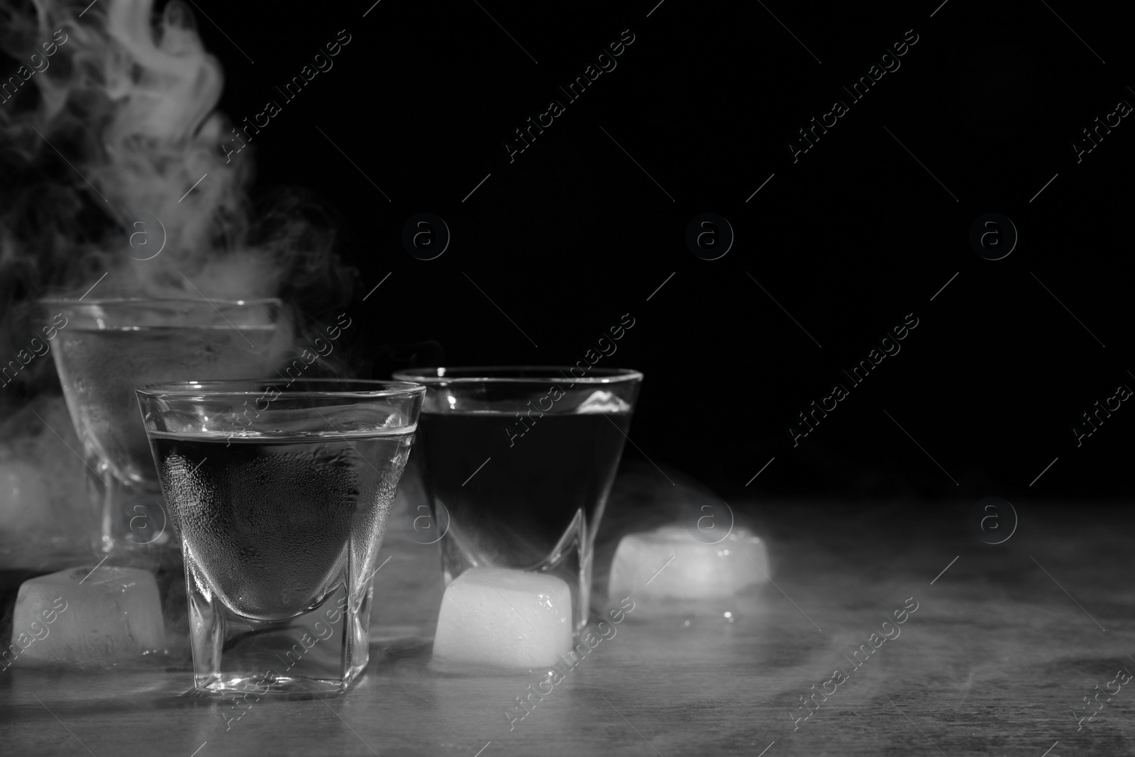 Photo of Vodka in shot glasses with ice on table against black background, space for text