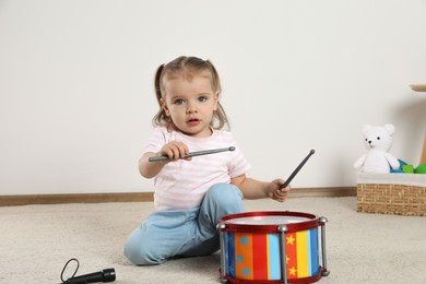 Cute little girl playing with drum and drumsticks at home