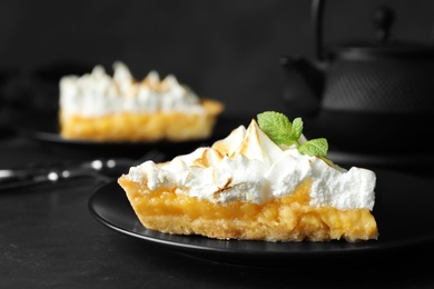 Plate with piece of delicious lemon meringue pie on black table