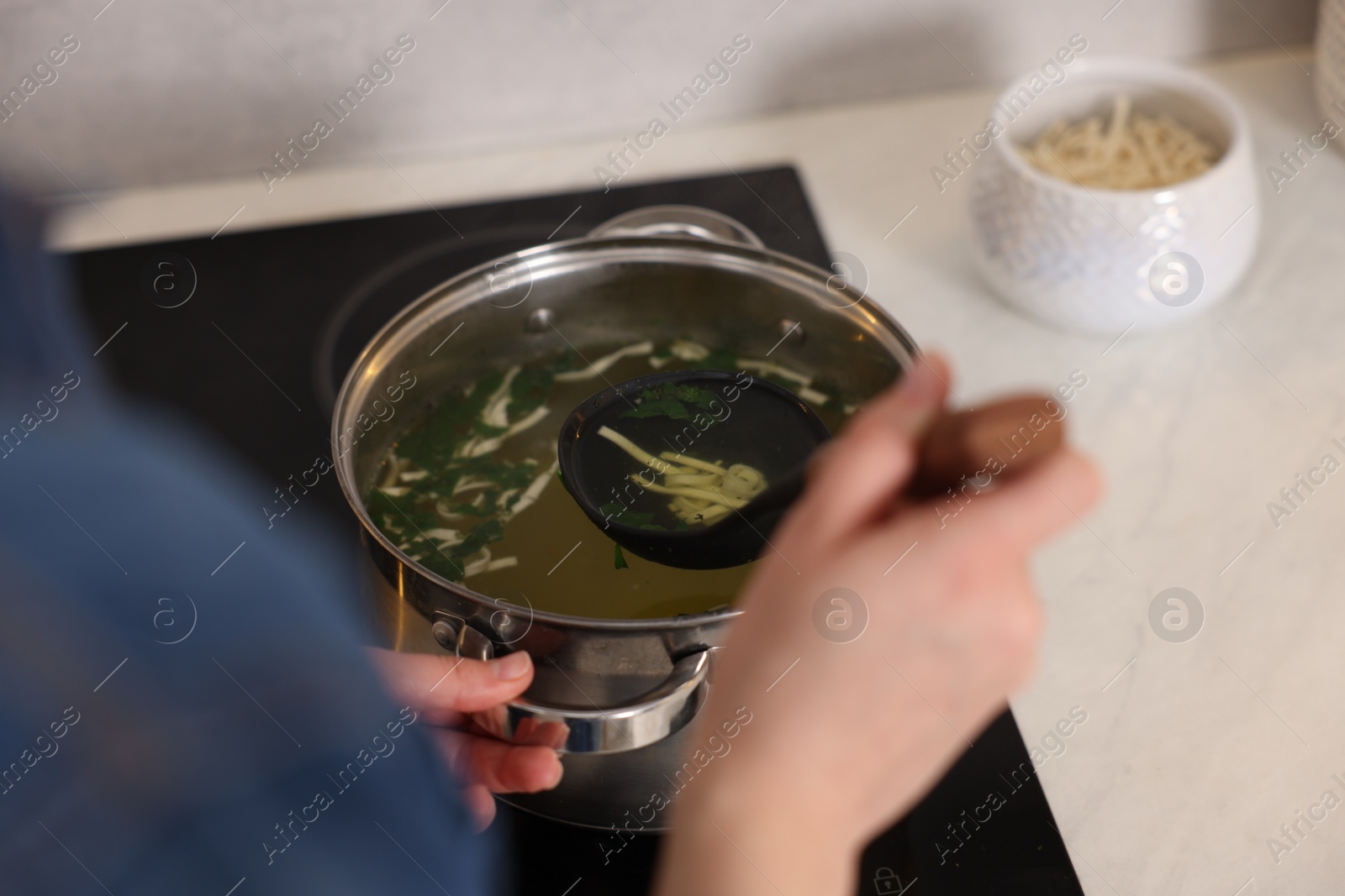 Photo of Woman cooking soup at countertop in kitchen, closeup