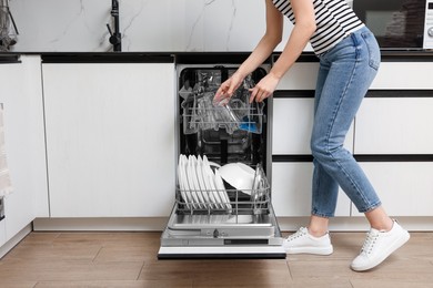 Photo of Woman loading dishwasher with glasses and plates in kitchen, closeup