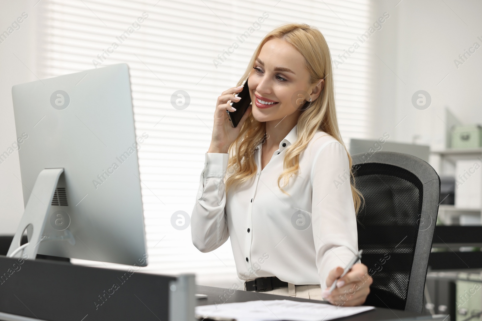 Photo of Secretary talking on smartphone at table in office