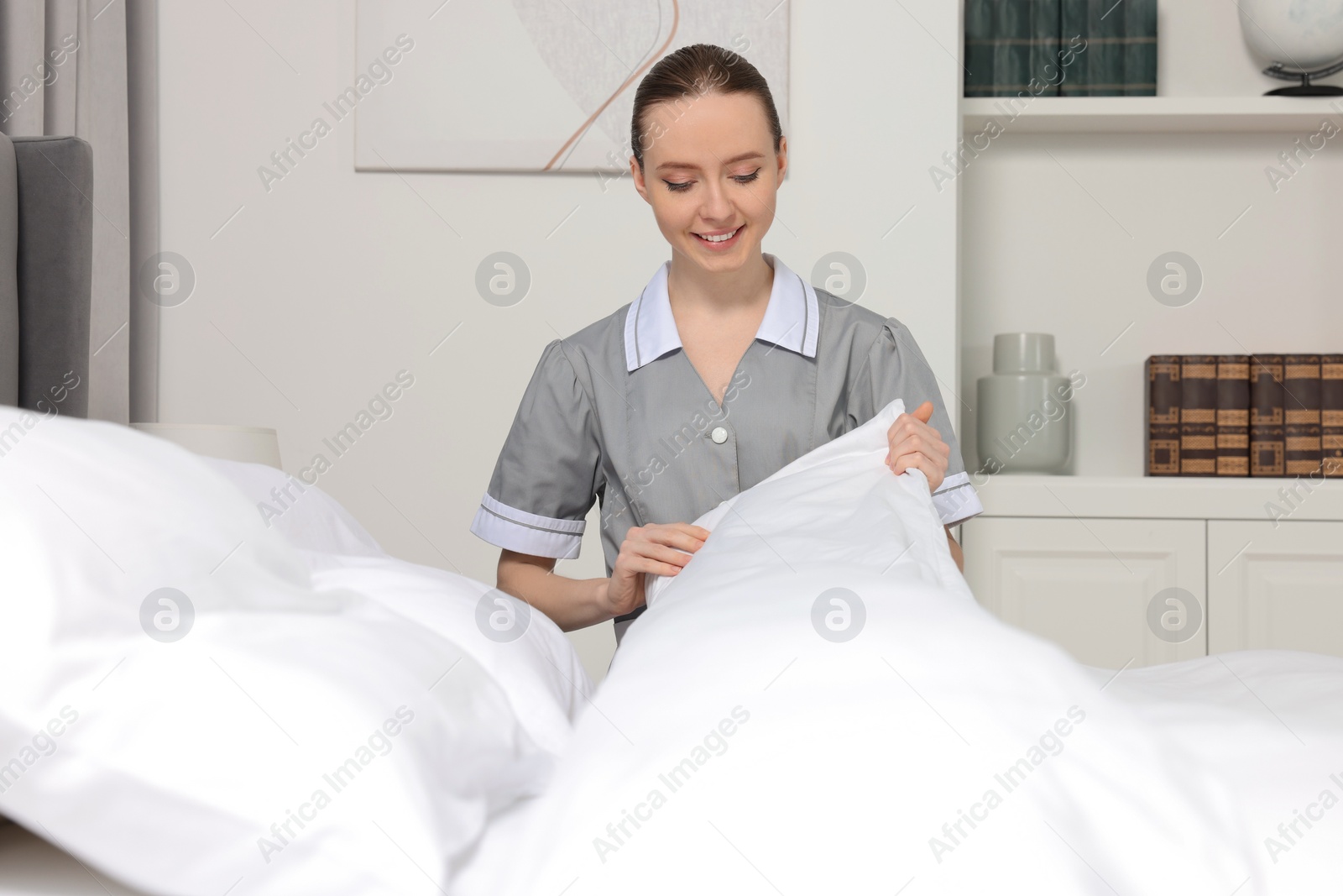 Photo of Young maid making bed in hotel room