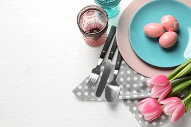 Photo of Festive Easter table setting with painted eggs on wooden background, top view. Space for text