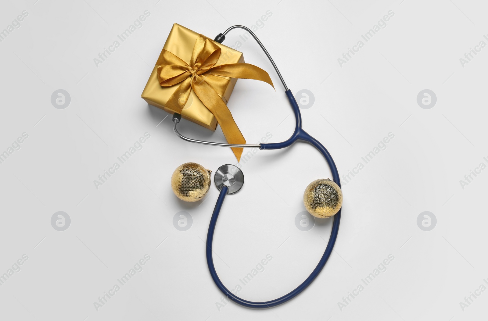 Photo of Greeting card for doctor with stethoscope, gift box and Christmas decor on white background, flat lay