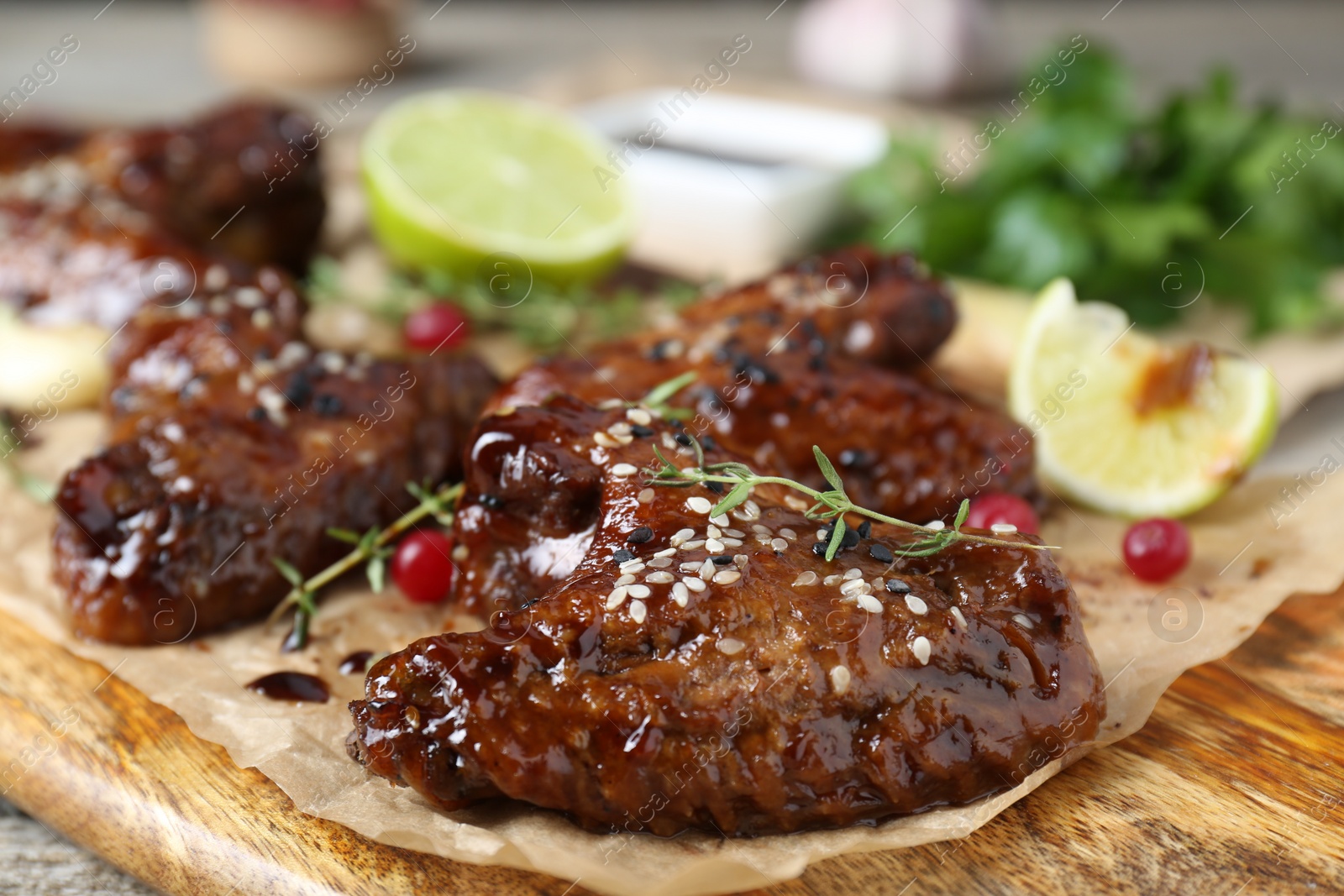 Photo of Tasty chicken wings glazed in soy sauce with garnish on wooden board, closeup