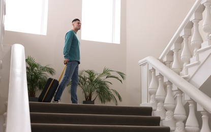 Photo of Handsome man with suitcase going up stairs in hotel