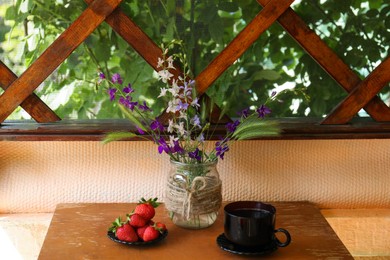 Bouquet of beautiful wildflowers, aromatic coffee and fresh strawberries on wooden table