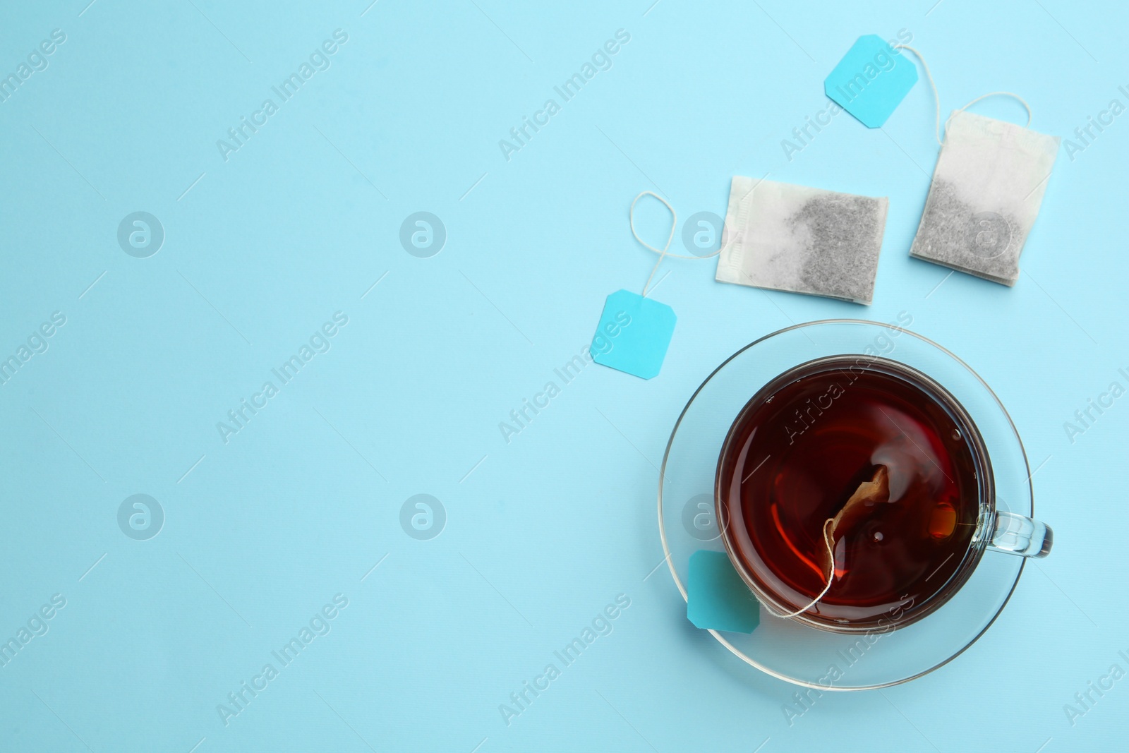 Photo of Tea bags and glass cup of hot drink on light blue background, flat lay. Space for text