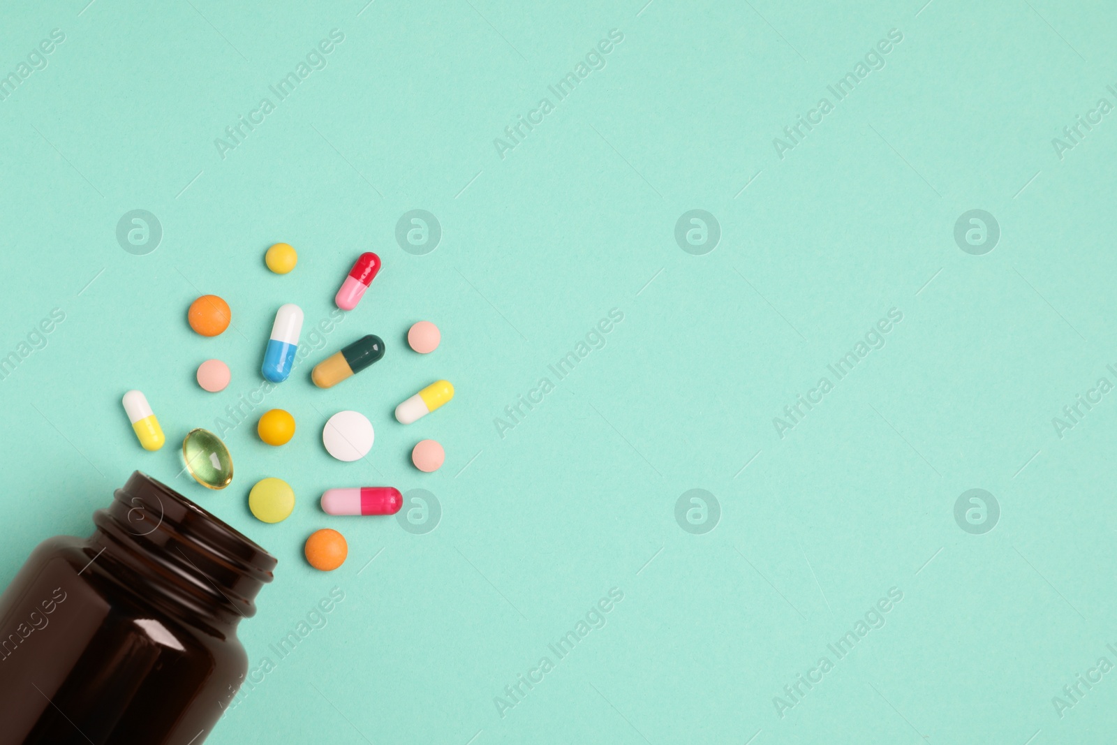 Photo of Plastic medical bottle with many different pills on turquoise background, flat lay. Space for text