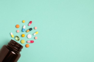 Plastic medical bottle with many different pills on turquoise background, flat lay. Space for text