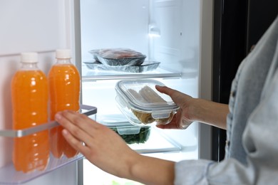 Photo of Young woman taking container with corn out of refrigerator, closeup